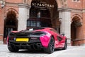 Bright pink McLaren luxury racing car parked outside the St. Pancras Renaissance Hotel in King\'s Cross, central London.