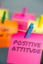 A bright pink sticky note with the text Positive Attitude hung from a clothesline by a blue clothespin.