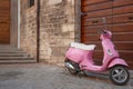 bright pink typically Italian motor-scooter parked by old door in street