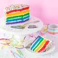 A bright rainbow birthday cake with a slice in front, ready for eating. Royalty Free Stock Photo