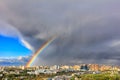 A bright rainbow in the sky above city houses after a thunderstorm separates thunderclouds from the clear sky