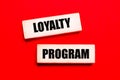 On a bright red background, there are two light wooden blocks with the text LOYALTY PROGRAM