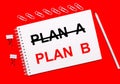 On a bright red background, a white pencil, white paper clips, and a white notebook with the text PLAN B Royalty Free Stock Photo
