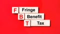 On a bright red background, wooden cubes and blocks with the text FBT Fringe Benefit Tax. Manufacturing of wooden toys Royalty Free Stock Photo