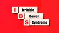 On a bright red background, wooden cubes and blocks with the text IBS Irritable Bowel Syndrome. Manufacturing of wooden toys