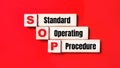 On a bright red background, wooden cubes and blocks with the text SOP Standard Operating Procedure. Manufacturing of wooden toys Royalty Free Stock Photo