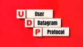On a bright red background, wooden cubes and blocks with the text UDP User Datagram Protocol. Manufacturing of wooden toys
