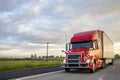 Bright red big rig bonnet semi truck transporting cargo in dry van semi trailer running on the evening highway road Royalty Free Stock Photo