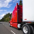 Bright red big rig long haul semi truck with high cabin transporting cargo in semi trailer driving on multiline road