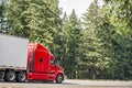 Bright red big rig long haul semi truck with refrigerator semi trailer moving on the road with green trees on the side Royalty Free Stock Photo