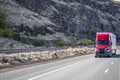 Bright red big rig long hauler semi truck with dry van semi trailer running on the road along the rocky mountain range Royalty Free Stock Photo