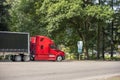 Bright red big rig semi truck with covered black semi trailer standing on the rest area parking lot parallel to the highway Royalty Free Stock Photo