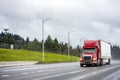 Bright red big rig semi truck with dry van semi trailer moving on the straight wide highway road with wet surface at rain weather Royalty Free Stock Photo