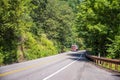 Bright red big rig semi truck transporting commercial cargo moving on the green forest winding road Royalty Free Stock Photo