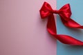 Bright red bow made from silk ribbon on blue and pink background. Festive concept with copy space on the left side. Birthday Royalty Free Stock Photo