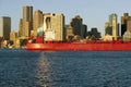 Bright red cargo ship travels in front of Boston Harbor and the Boston skyline at sunrise as seen from South Boston, Massachusetts