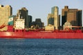 Bright red cargo ship travels in front of Boston Harbor and the Boston skyline at sunrise as seen from South Boston, Massachusetts Royalty Free Stock Photo