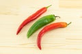 Bright red chili peppers and green pod lie in parallel on a wooden background