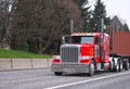 Bright red classic big rig semi truck transporting container on