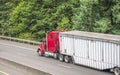 Bright red classic big rig semi truck transporting industrial cargo in covered bulk semi trailer running on the turning road with Royalty Free Stock Photo
