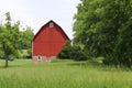 Bright red farm barn with fresh painted white trim in a natural field with trees and agriculture beyond Royalty Free Stock Photo