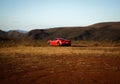 Bright red Ferrari car parked on a lush green grass field with majestic mountains in the background.