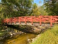 Bright red foot bridge over a slow moving stream creek in a wooded park in daylight Royalty Free Stock Photo
