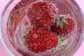 Bright red fresh strawberries with green leaves, floating in sparkling water in a glass and covered with bubbles. Royalty Free Stock Photo