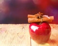 Red glossy apple cinnamon sticks tied with twine anise star on wooden table in glittering garland bokeh lights. Christmas Royalty Free Stock Photo