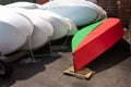 Bright red and green sailboat hull alongside stacked white fiberglass sailboat hulls