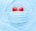 Bright red heart on a pile of medical face masks. Concept of support, love, care and a thank you to the frontline essential