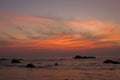 A bright red lines of clouds in the dark blue sky of sunset against the evening sea and rocks Royalty Free Stock Photo