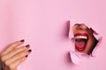 Bright red lips through torn pink paper background. Surprised girl, emotions. Make up artist, beauty concept. Ready to party.