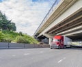 Bright red long haul diesel big rig semi truck with dry van semi trailer running on the straight highway road under the bridge Royalty Free Stock Photo