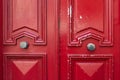 Bright red painted wooden door with geometric frames and peeling paint. Symmetric double door decorations and two old metal handle Royalty Free Stock Photo