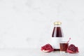 Bright red pomegranate juice in glass bottle mock up with blank label, straw, wine glass, fruit grains on white wood table. Royalty Free Stock Photo