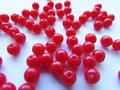 Bright red round beads for needlework are randomly scattered over a white background