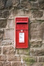 Bright red Royal Mail ER letter post box with royal crown logo in old historic dry stone wall rural location. Royalty Free Stock Photo