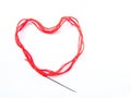 Bright red scarlet wool thick thread with a sewing needle lies in the shape of a heart object on a white background Royalty Free Stock Photo