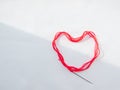 A bright red scarlet woolen thick thread with a sewing needle lies in the shape of a heart, lit on the white background Royalty Free Stock Photo