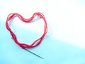 A red woolen thick thread with a sewing needle lies in the shape of a heart, lit on the white and blue background Royalty Free Stock Photo