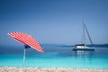 Bright red striped sun beach umbrella on pebble beach against turquoise blue shellow sea water and clean blue sky. White Royalty Free Stock Photo