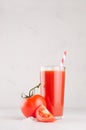 Bright red tomato cocktail in elegance glass with glossy tomatoes, salt, straw and ripe piece on white wooden board, vertical. Royalty Free Stock Photo