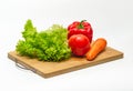 Bright red tomato, green salad, bell pepper, carrot on a board. Vegan food. Salad preparation Royalty Free Stock Photo