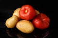 Bright red tomatoes and potatoes on a black background, vegetarianism Royalty Free Stock Photo