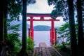 Bright red Torii gate submerged in the waters of Ashi lake, caldera with mountains on the background. Hakone Shrine