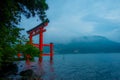 Bright red Torii gate submerged in the waters of Ashi lake, caldera with mountains on the background. Hakone Shrine, Kanagawa pref