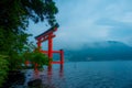 Bright red Torii gate submerged in the waters of Ashi lake, caldera with mountains on the background. Hakone Shrine, Kanagawa pref