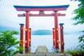 Bright red Torii gate submerged in the waters of Ashi lake, caldera with mountains on the background. Hakone Shrine, Kanagawa pref