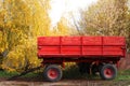 Bright red tractor trailer on a background of yellow leaves. Rural, rustic autumn landscape